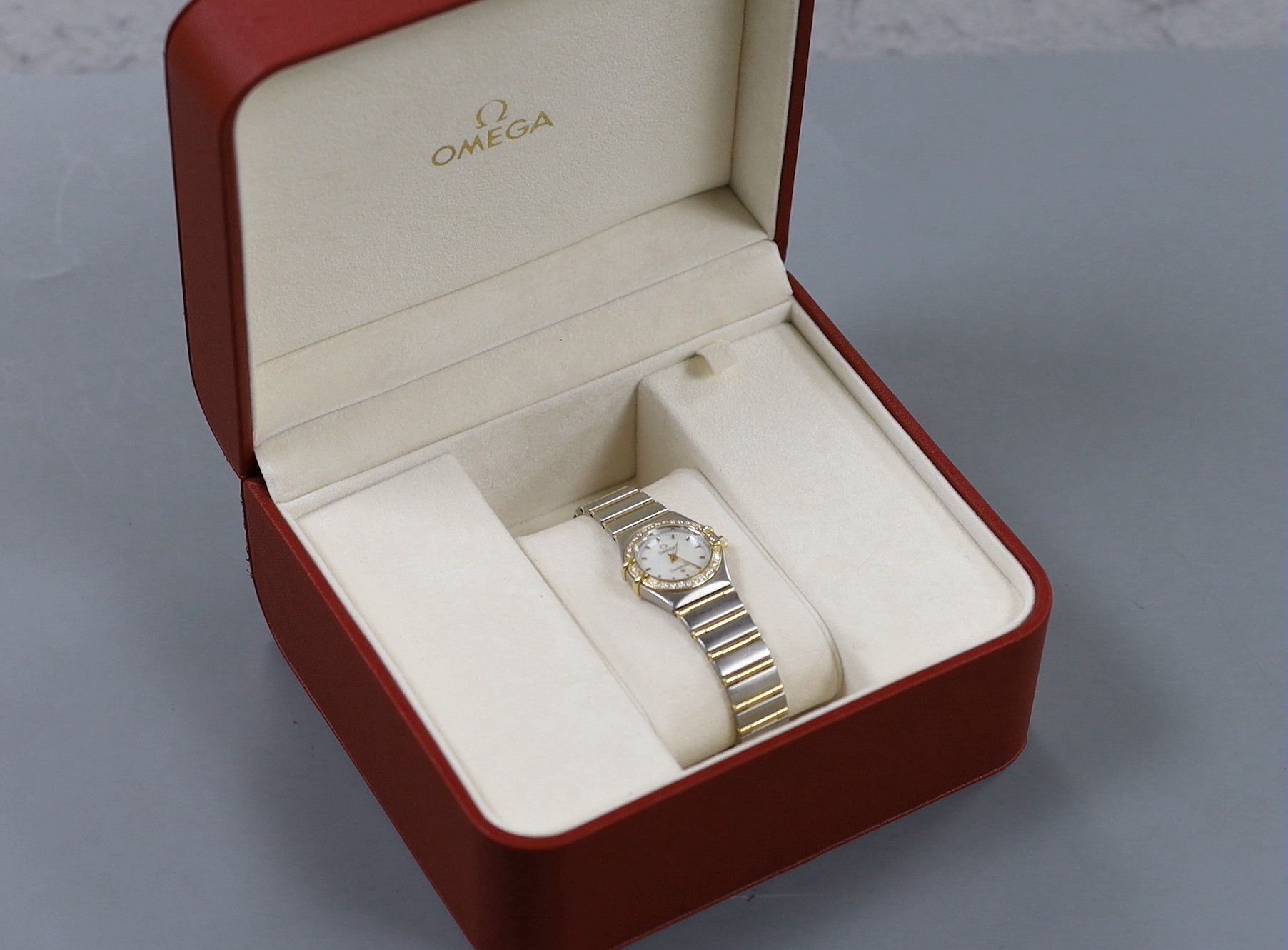 A lady's modern steel and yellow metal Omega Constellation quartz wrist watch and bracelet, with mother of pearl dial and diamond set bezel, with box and some papers, including precious gem certificate